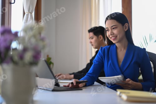 Preview: Attractive businesswoman working with computer tablet while sitting with her colleague in office.
