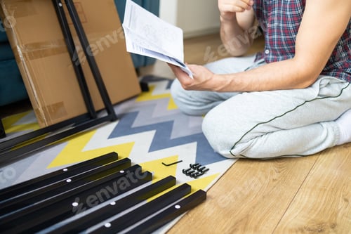 Preview: Man assembling furniture at home in the living room. Young man sitting on the floor and reading inst
