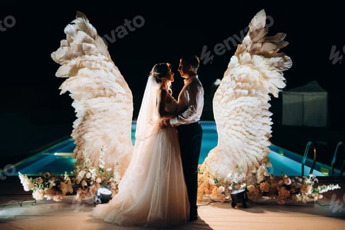 Preview: cutting the wedding cake against the backdrop of white wings