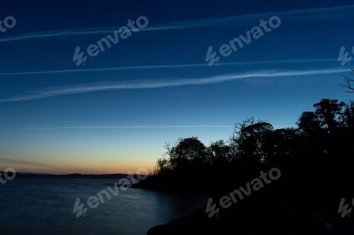 Preview: Serene twilight landscape with silhouetted trees by the water and streaks of clouds in the sky