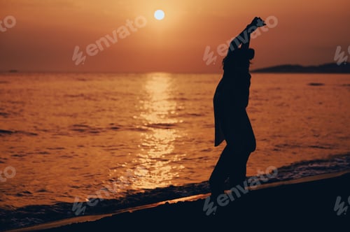 Preview: Silhouette of an attractive young woman posing on the beach during sunset