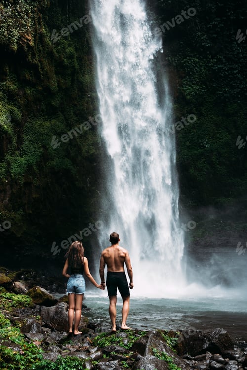 Preview: A man holds the hand of a beautiful woman at a waterfall. A couple in love on a waterfall