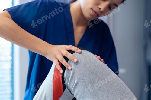 Preview: Smiling diverse female physiotherapist treating knee of senior male patient in therapy, copy space