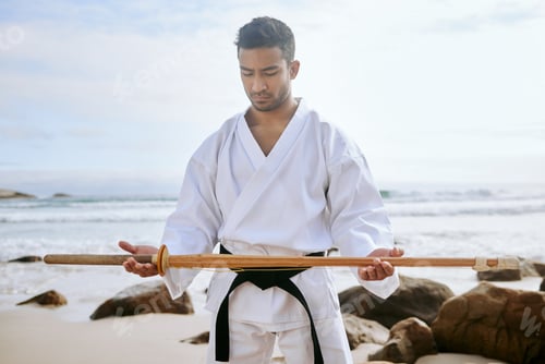 Preview: Shot of a young martial artist practising karate with a wooden katana on the beach