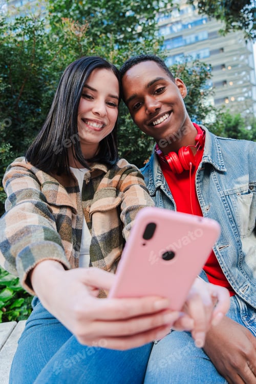 Preview: Vertical. Young multiracial couple enjoys browsing the internet on a cellphone. Two teenage friends