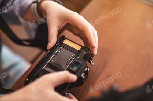Preview: Close-up hands of woman putting a roll of film into a retro camera on brown wooden table in the