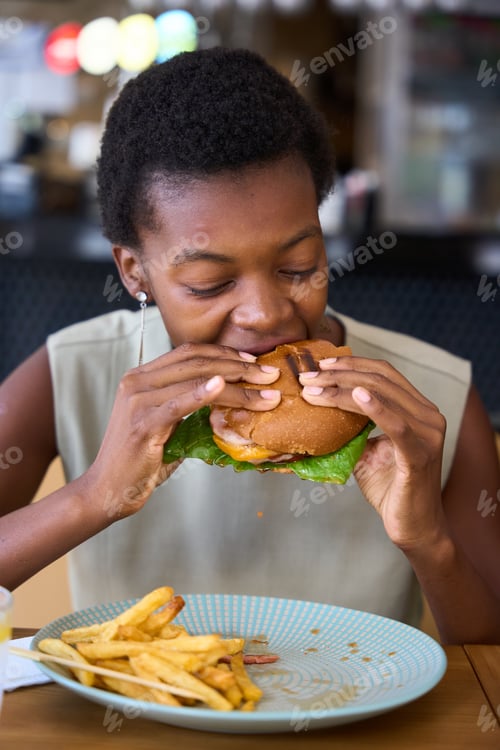 Preview: Young woman enjoying eating a delicious burger and fries