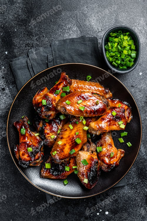 Preview: Baked chicken wings with sweet chili sauce in a plate. Black background. Top view