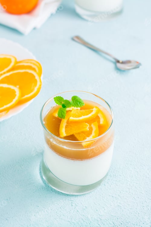 Preview: Homemade panna cotta with orange and mint leaf in a glass on a light table. Sweet Italian dessert.