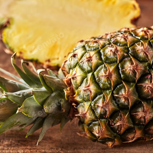 Preview: Closeup of whole and half juicy healthy pineapple presented on a kitchen board on a wooden table