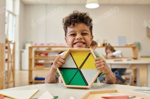 Preview: positive african american boy holding wooden didactic materials in blurred montessori school