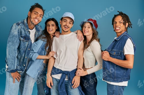 Preview: diverse group of excited interracial friends in trendy and denim clothes looking at camera on blue