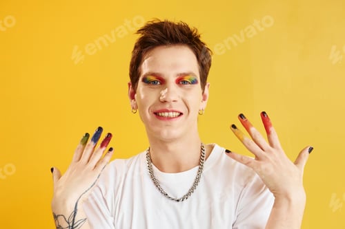 Preview: Young gay man is standing in the studio and posing for a camera. Rainbow make up