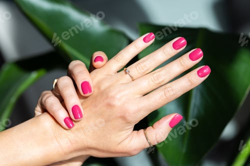 Preview: Close-up beautiful female hand with pink nails on green background.