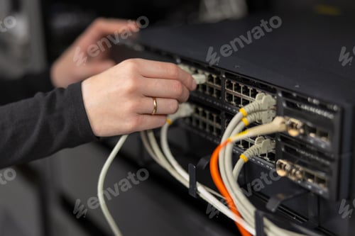 Preview: Female IT technician in a datacenter connecting and configuring network switches with cables