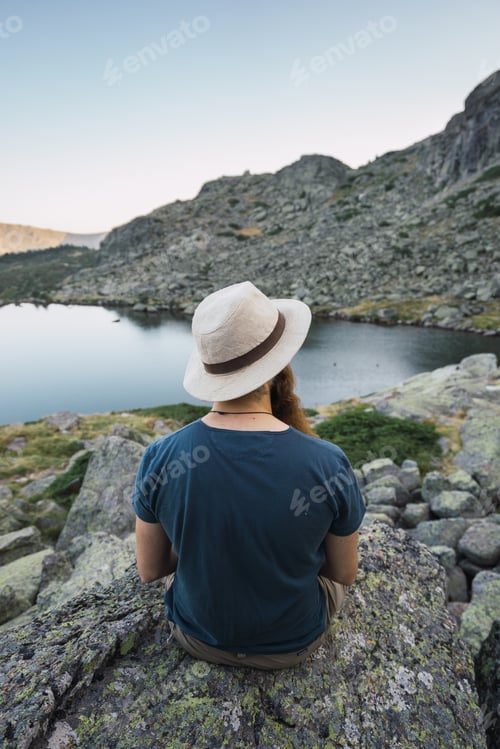 Preview: Young man sitting on rocks near lake