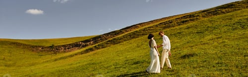 Preview: beautiful landscape, just married couple walking in green field, young newlyweds on hills, banner
