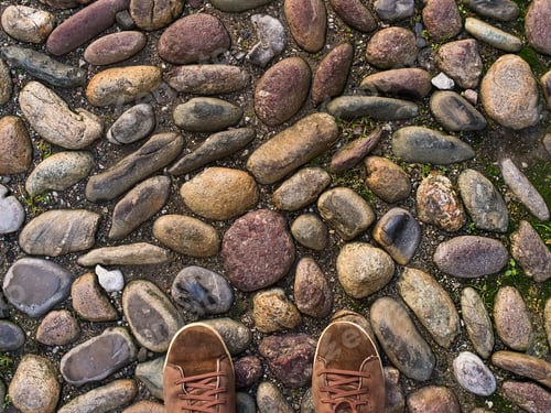 Preview: Feet in brown sneakers on the old medieval stone pavement.