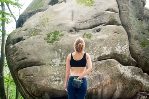 Preview: young woman with climbing equipment in front of a stone