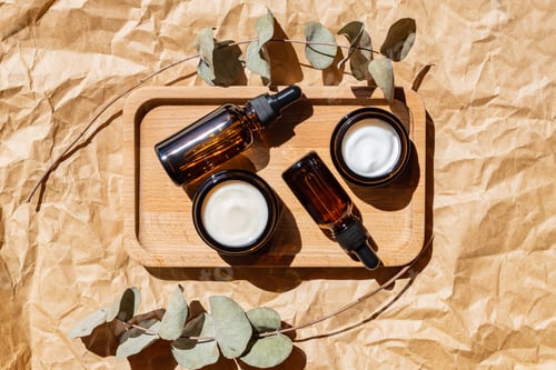 Preview: Dark glass cosmetic bottles with a dropper and face cream on a craft paper with eucalyptus leaves.