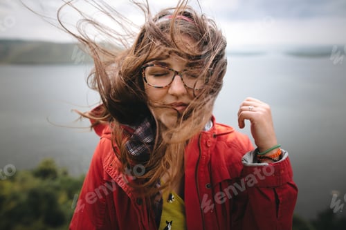 Preview: Traveler girl in red raincoat and with windy hair standing on top of rock mountain