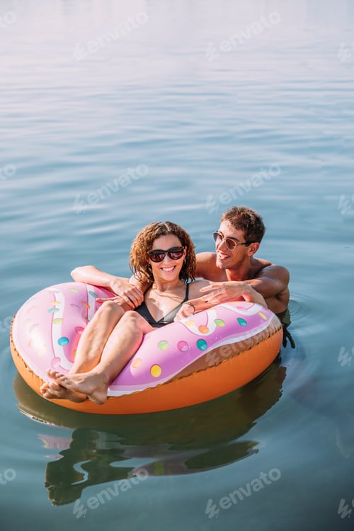 Preview: Happy young couple bathing in the sea on inflatable float in donut shape