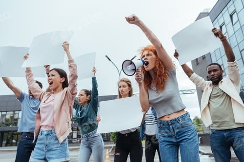 Preview: emotional redhead woman screaming in megaphone near multicultural people