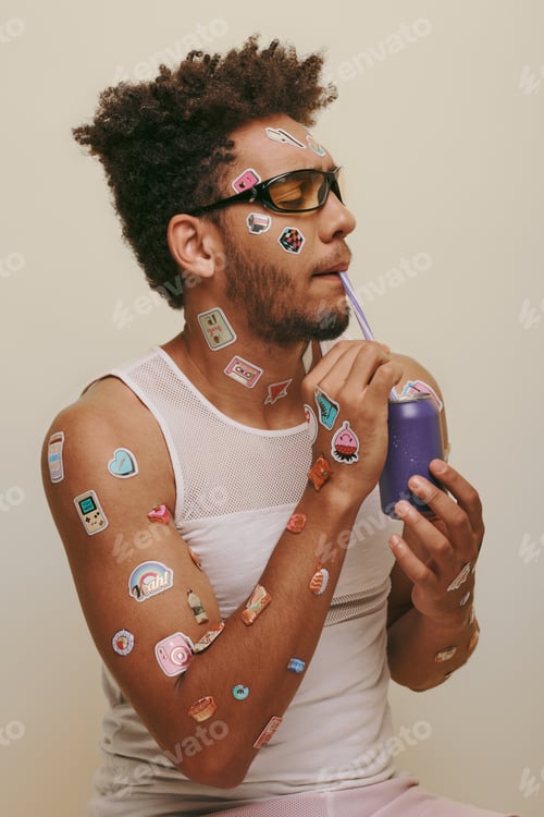 Preview: curly african american man with stickers on face and body drinking soda on grey background