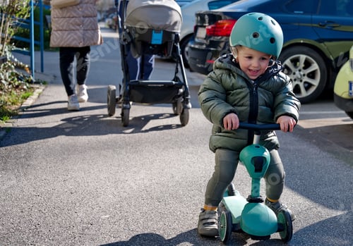 Preview: Little toddler on scooter and his parents with baby stroller walking down the street