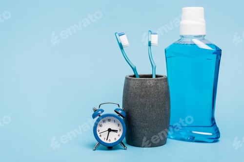Preview: Toothbrushes near mouthwash and small alarm clock on blue background