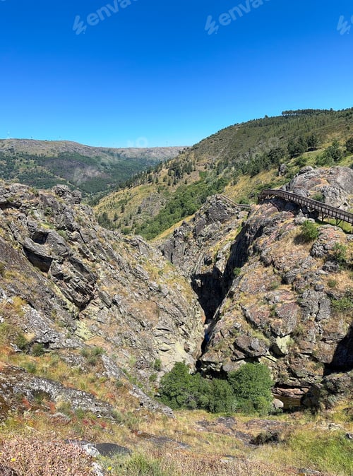 Vista previa: A serene valley with a wooden path, embraced by rocky cliffs