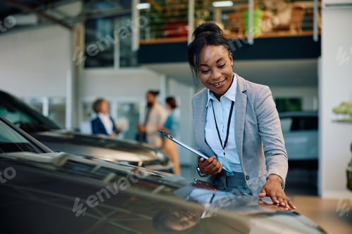 Preview: Happy black car saleswoman working in showroom.