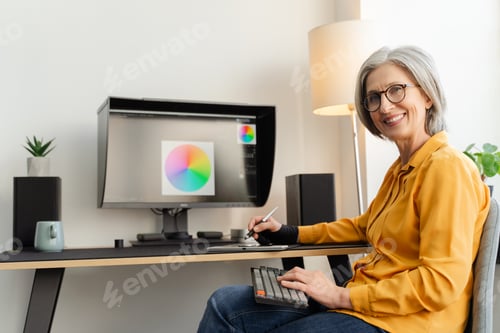 Preview: Smiling graphic designer, retoucher using graphic tablet. Senior woman, freelancer working in office