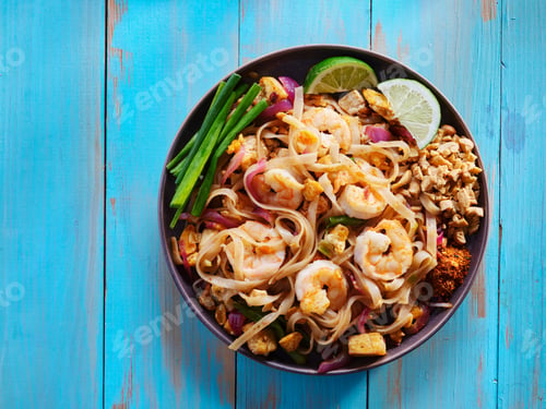 Preview: shrimp pad thai on plate in flat lay composition with copy space atop of colorful wooden table