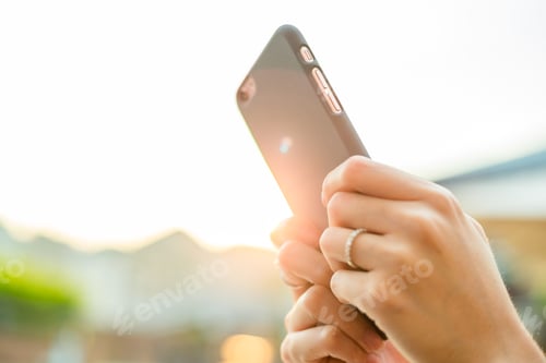 Preview: Woman using mobile phone with sun flare