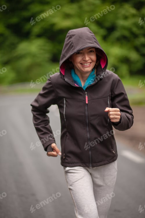 Preview: One Cheerful Mature Woman, Jogging Outdoors On A Asphalt Road, In A Nature. Wearing Sport Clothing