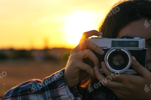 Preview: Young woman taking photos with analog camera in the field at sunset
