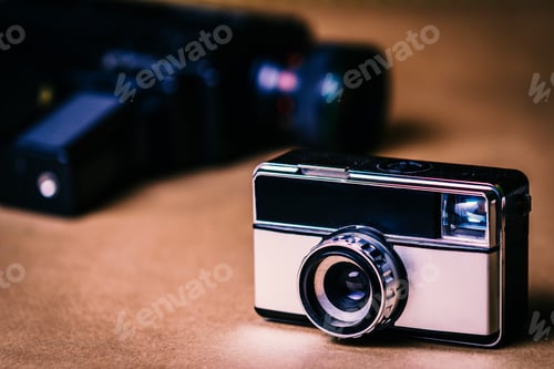 Preview: Vintage gray photo camera with brown background with an unfocused video camera.