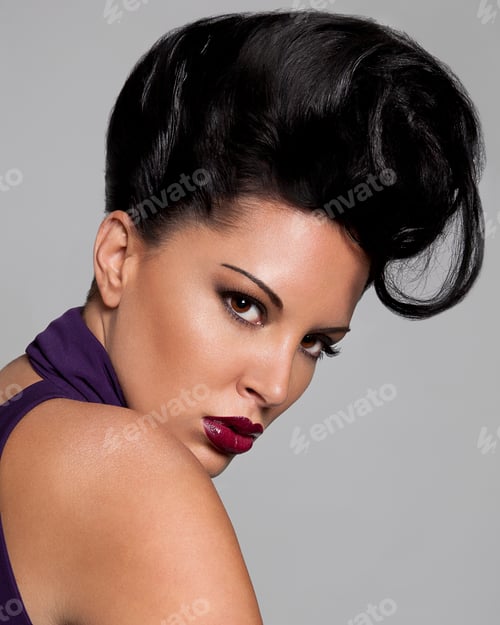 Preview: Woman with dramatic makeup and an elaborate hairstyle posing against a gray background.