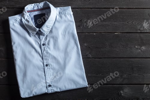 Preview: Light Blue Shirt Folded on Dark Wood Surface