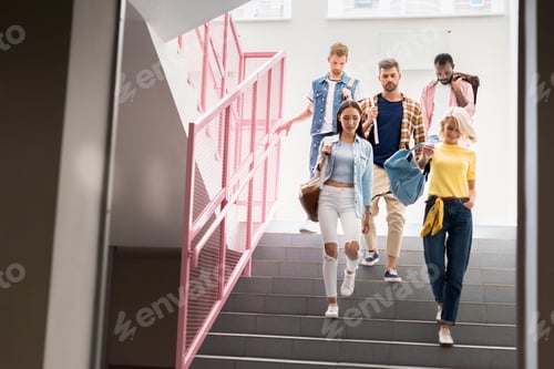 Preview: stylish young students walking down on stairs of college corridor