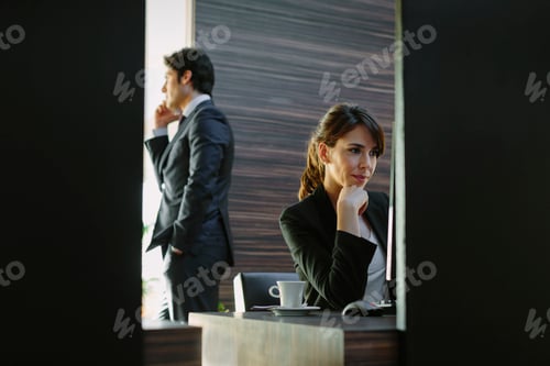Preview: Businesswoman pondering at her desk as her colleague walks by
