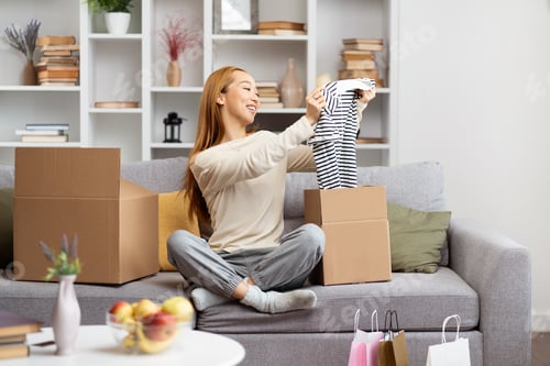 Preview: Happy Young Woman Unpacking Clothes in New Home