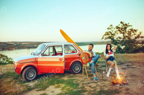 Preview: Couple sitting and resting on the beach playing guitar on a summer day near river