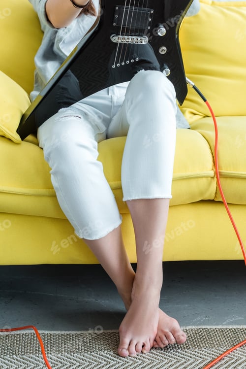 Preview: cropped view of girl sitting on yellow sofa with electric guitar
