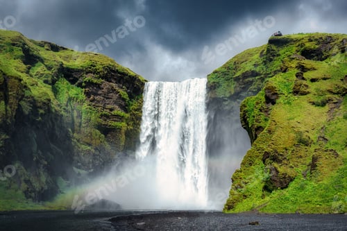 Preview: Majestic Skogafoss waterfall flowing with rainbow and moody sky in summer at Iceland
