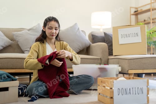 Preview: Woman asian holding donation box full with clothes and select clothes. Concept of donation and