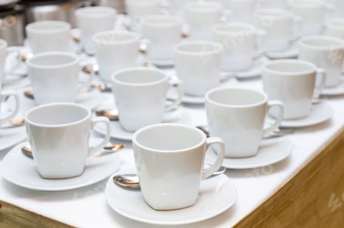 Preview: Many rows of white coffee cup with saucer and teaspoon on table and coffee maker background