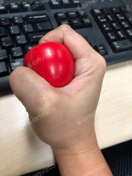Preview: A hand squeezing a stress ball while at work in the office to manage emotional stress.