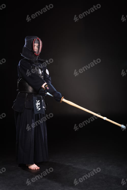 Preview: Full length view of kendo fighter in armor practicing with bamboo sword on black
